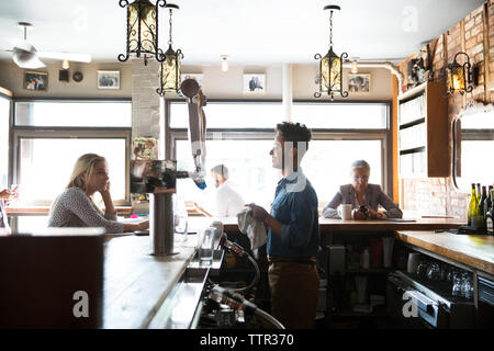 Lächelnd Eigentümer im Gespräch mit Kunden beim Stehen an der Theke im Cafe Stockfoto