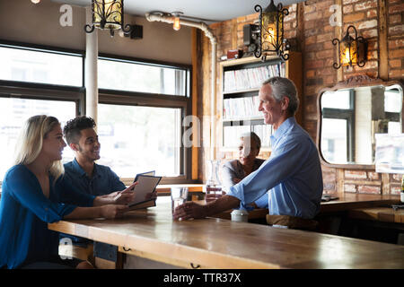 Männliche Inhaber, die Getränke beim Gespräch mit dem Kunden an Theke im Cafe Stockfoto