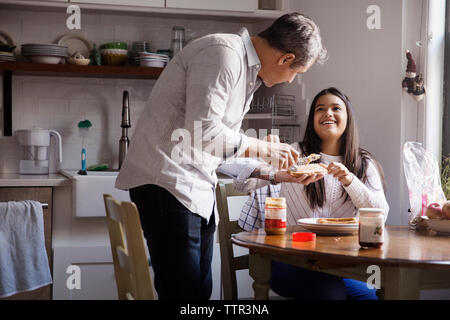 Lächelnde Mädchen an Vater Anwendung Peanut Butter auf Brot in der Küche Stockfoto