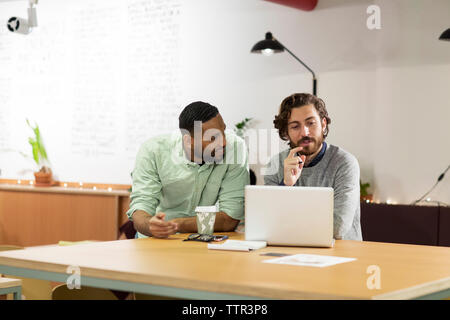 Geschäftsmann diskutiert mit Kollegen, während er im Büro einen Laptop benutzt Stockfoto