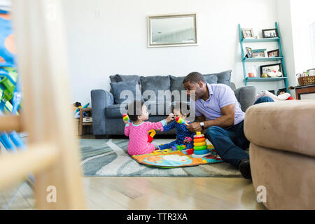 Vater spielen mit Töchtern während auf dem Teppich zu Hause sitzen Stockfoto