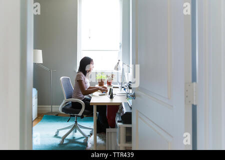 Frau arbeiten auf dem Desktop Computer zu Hause Büro durch Tür gesehen Stockfoto
