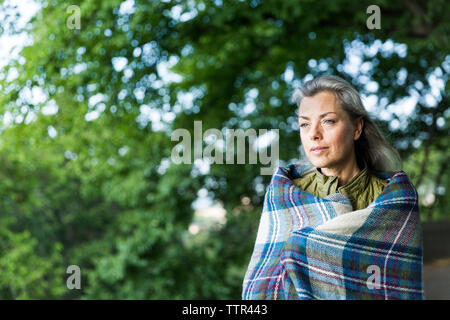 Nachdenkliche Frau, die in der Decke eingewickelt, wenn Sie auf der Suche gegen Filialen Stockfoto