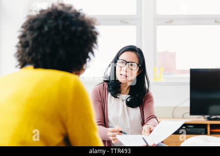Geschäftsfrau, die Dokumente einer Kollegin während ihrer Arbeit zeigt Stockfoto