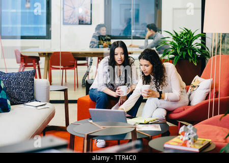 Geschäftsfrauen diskutieren über Laptop, während männliche Kollegen im Büro im Hintergrund planen Stockfoto