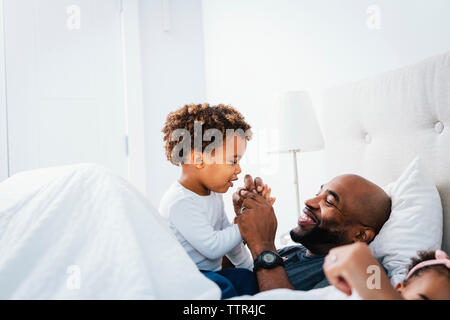 Gerne Vater mit Sohn, während sie sich auf dem Bett gegen die Wand zu Hause Stockfoto