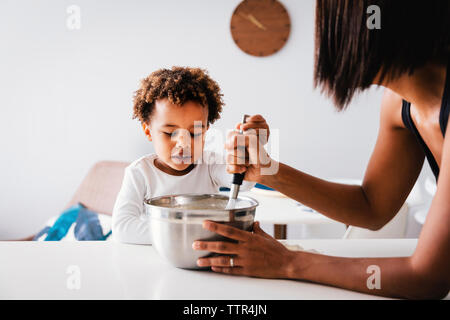 Sohn mit Mutter vermischen Teig in der Schüssel auf Küche Insel zu Hause. Stockfoto