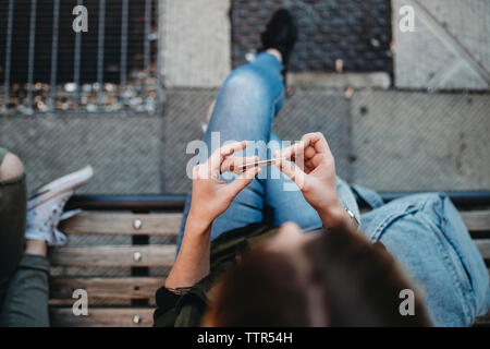 Junge Frau rolling Zigarette auf der Bank sitzen Stockfoto