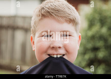 Junge lächelnd mit seinem T-Shirt in seinem Mund im Hinterhof Stockfoto