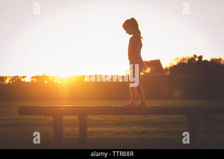 Seitenansicht der jungen Mädchen zu Fuß auf Spielgeräte bei Sonnenuntergang Stockfoto