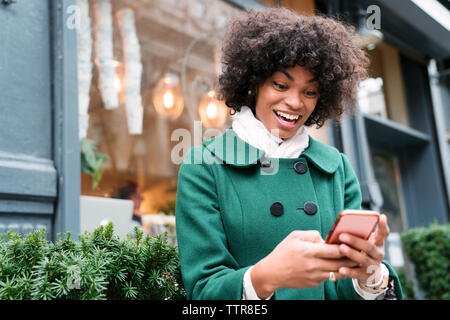 Happy Geschäftsfrau mit Smart Phone, während gegen den Bau in der Stadt stehend Stockfoto