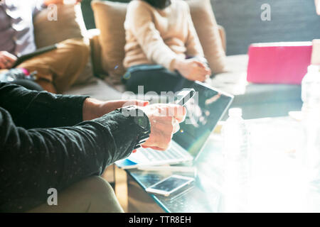 Zugeschnittenes Bild der Geschäftsmann mit Smart Phone während der Sitzung mit den Kollegen im Büro Stockfoto