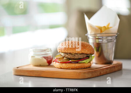 Leckere Burger mit Pommes frites und Sauce auf Holz Schneidebrett Stockfoto