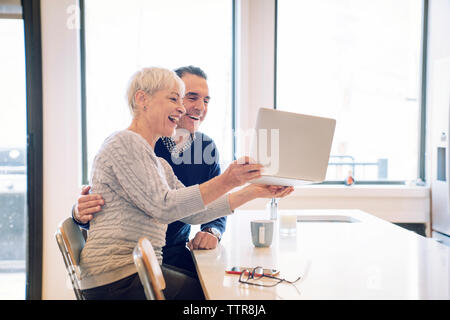 Gerne ältere Frau mit Laptop Computer, während der Mann am Tisch sitzen Stockfoto