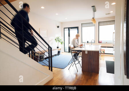 Mann Treppe hinunter, während Frau mit Laptop am Tisch in Home Stockfoto