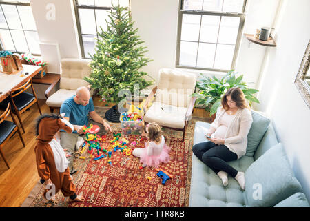 Hohe Betrachtungswinkel von Vater spielen mit den Kindern während der Schwangerschaft Frau sitzt auf einem Sofa Stockfoto