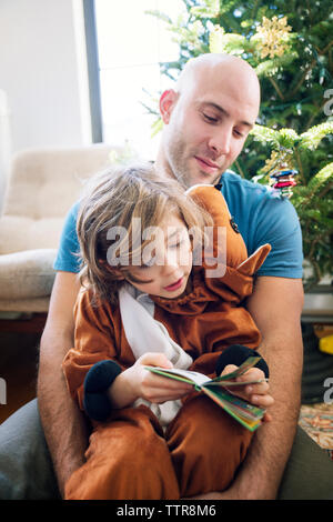 Vater sitzt mit Sohn im Kostüm vor dem weihnachtsbaum zu Hause Stockfoto