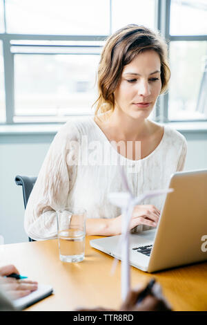 Geschäftsfrau, die einen Laptop benutzt, während sie am Schreibtisch im Büro arbeitet Stockfoto