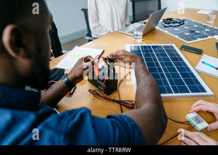 Nahaufnahme der Geschäftsmann Befestigung metall Clips über den Akku während der Arbeit mit Solarpanel Modell Stockfoto