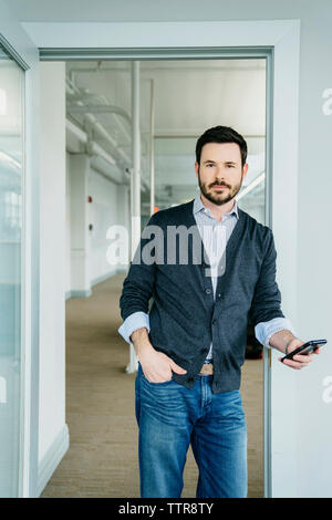 Portrait von Geschäftsmann holding Telefon beim Stehen an der Tür im Büro Stockfoto