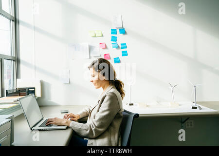 Seitenansicht des Geschäftsfrau mit Laptop während der Arbeit, die von der WEA-Modelle auf dem Schreibtisch angeordnet Stockfoto
