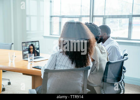 Geschäftsleute Videokonferenzen mit Geschäftsfrau über Laptop im Sitzungsraum mit Blick durch Glas Stockfoto