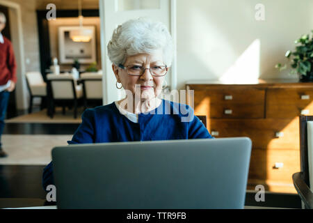 Ältere Frau mit Laptop zu Hause mit älterer Mann im Hintergrund Stockfoto