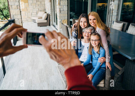 7/8 die Hände älterer Mann fotografieren Happy Family durch Smart Phone auf der Veranda Stockfoto