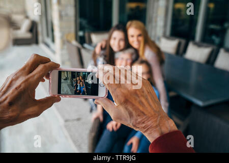 7/8 die Hände älterer Mann fotografieren Familie durch Smart Phone auf der Veranda Stockfoto