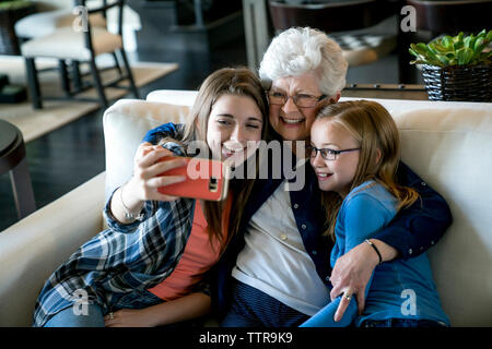 Hohe Betrachtungswinkel von Happy Großmutter und Enkelinnen unter selfie durch Smart Phone beim Sitzen auf dem Sofa Stockfoto