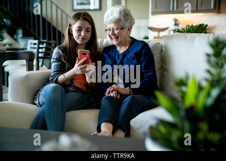 Enkelin, Smart Phone zu Großmutter beim Sitzen auf dem Sofa zu Hause Stockfoto