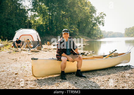 Portrait von Mitte nach Mann sitzt auf dem Boot mit Freunden im Hintergrund auf einem Campingplatz Stockfoto