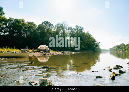 Mittlere Entfernung Anzeigen von Freunden sprechen beim Sitzen auf einem Campingplatz am See gegen Sky Stockfoto