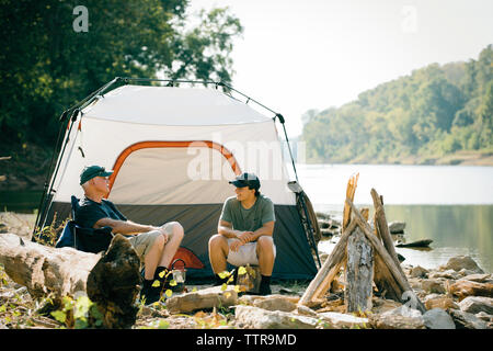 Freunde sprechen, während Sie sich auf einem Campingplatz am See gegen Sky Stockfoto