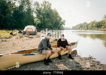 Männliche Freunde sprechen während der Sitzung auf dem Boot am Seeufer gegen Sky Stockfoto