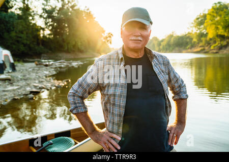 Portrait von älteren Mann mit Hände auf Hüfte stehen mit dem Boot am Seeufer bei Sonnenuntergang Stockfoto