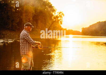 Älterer Mann angeln beim Stehen in der See gegen Himmel bei Sonnenuntergang Stockfoto