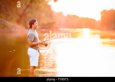 Seitenansicht des jungen Mann angeln beim Stehen in der See bei Sonnenuntergang Stockfoto