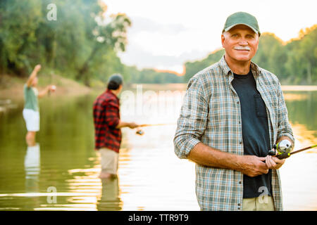 Portrait von lächelnden älteren Mann angeln mit Freunden in See gegen Sky Stockfoto