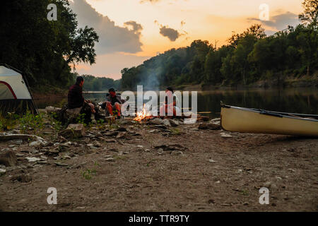 Freunde sprechen beim Sitzen auf einem Campingplatz gegen Himmel bei Sonnenuntergang Stockfoto