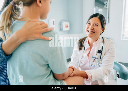 Fröhlich Kinderarzt holding Girl's Hand sitzt von Mutter im Untersuchungsraum Stockfoto