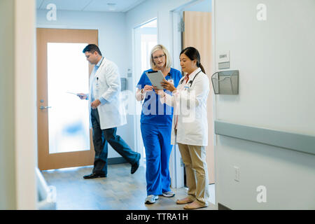 Weibliche Ärzte diskutieren über Tablet Computer während männliche Kollegen zu Fuß durch im Krankenhaus Stockfoto