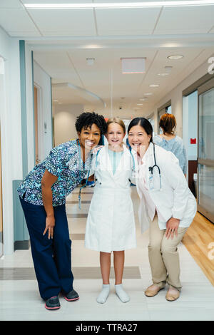 Volle Länge Portrait von fröhlichen Ärztinnen mit Mädchen tragen Laborkittel im Krankenhaus Flur Stockfoto