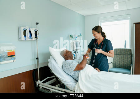 Krankenschwester handshaking mit älteren Patienten liegend auf Bett im Krankenhaus Stockfoto