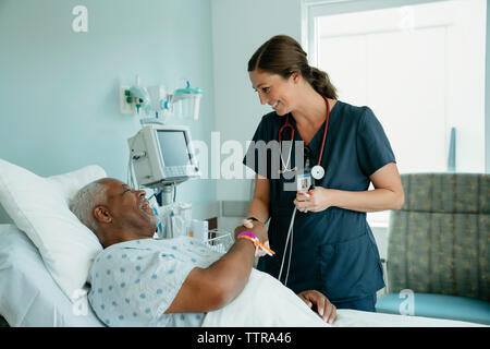 Lächelnd Krankenschwester handshaking mit älteren Patienten liegend auf Bett im Krankenhaus Stockfoto
