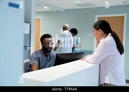 Arzt zu sprechen Männliche Krankenschwester im Krankenhaus Empfang, während Kollege mit Patienten laufen im Hintergrund Stockfoto