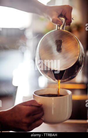 Zugeschnittenes Bild von Barista gießen Kaffee in der Tasse im Cafe Stockfoto