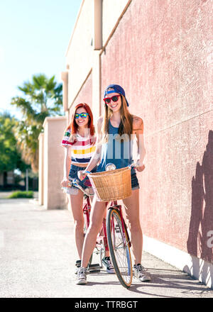 Portrait von Happy weibliche Freunde auf tandem Fahrrad am Bürgersteig gegen die Wand Stockfoto