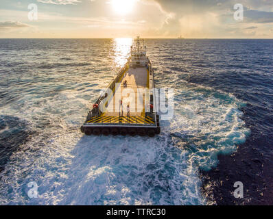 Hohe Betrachtungswinkel der Arbeiter auf Container schiff Segeln im Meer bei Sonnenuntergang Stockfoto