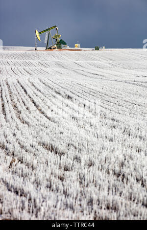 Mitte der Abstand von pumpjack am Ölindustrie über Feld gegen Himmel im Winter Stockfoto